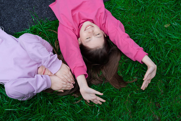 Twee mooie millennial kids vrienden liggend op groen gras in park of gazon. Blanke meisjes die samen lachen en plezier hebben. van bovenaf bekeken. - Foto, afbeelding