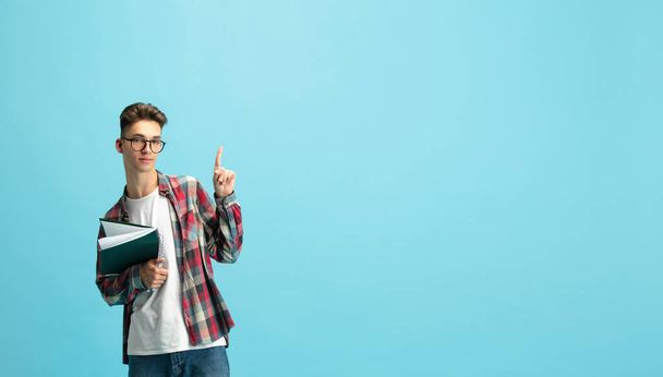 Half length portrait of young caucasian guy, student with notepad isolated over light blue studio background. - Valokuva, kuva