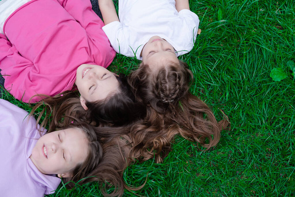 drie mooie meisjes liggen op groen gras. zusterschap, vriendschap, bff. zomertijd. - Foto, afbeelding