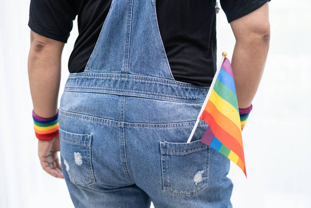 ゲイ、レズビアン、バイセクシャル、トランスジェンダー、人権の6月の社会でゲイ、レズビアン、バイセクシャル、トランスジェンダー、人権の毎年恒例のLGBTプライド月間のシンボルである、青いジーンジャケットやデニムシャツを着て虹色の旗を持っているアジアの女性. - 写真・画像