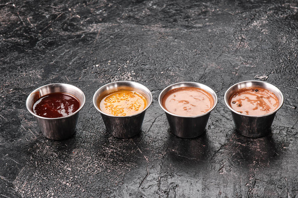 Set van verschillende sauzen in metalen saus kommen geïsoleerd op getextureerde zwarte achtergrond. Ruimte voor tekst - Foto, afbeelding