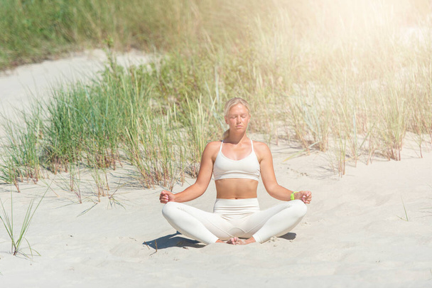 Femme pratiquant le yoga sur une dune de sable sur la plage - Photo, image