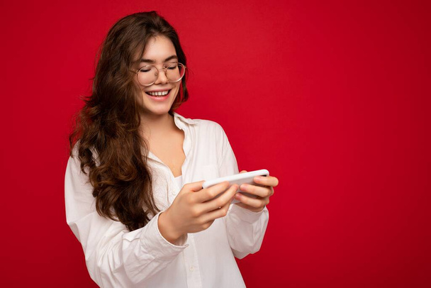 Kuva laukaus houkutteleva positiivisen näköinen nuori nainen yllään rento tyylikäs asu valmis eristetty taustalla tyhjä tila tilalla kädessä ja käyttämällä matkapuhelin viestien sms tarkastellaan - Valokuva, kuva