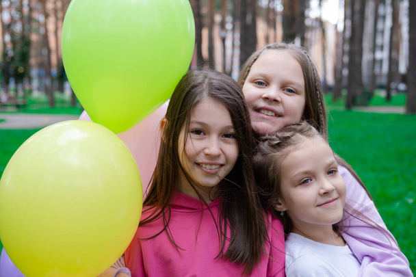drei hübsche Mädchen in bunten Kleidern, die sich in der Nähe von Heißluftballons umarmen. Geschwisterlichkeit, Freundschaft, bff. Sommerzeit. - Foto, Bild