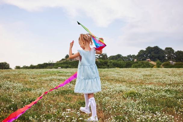 Full length of a young running girl with flying kite in the field in a blue dress - Valokuva, kuva