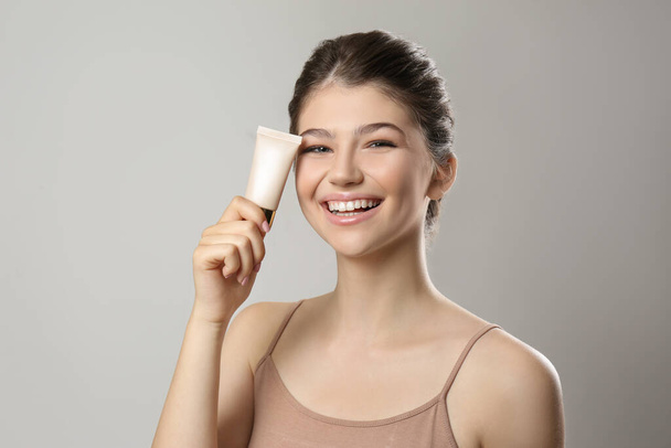 Beautiful girl with tube of foundation on light grey background - Foto, immagini