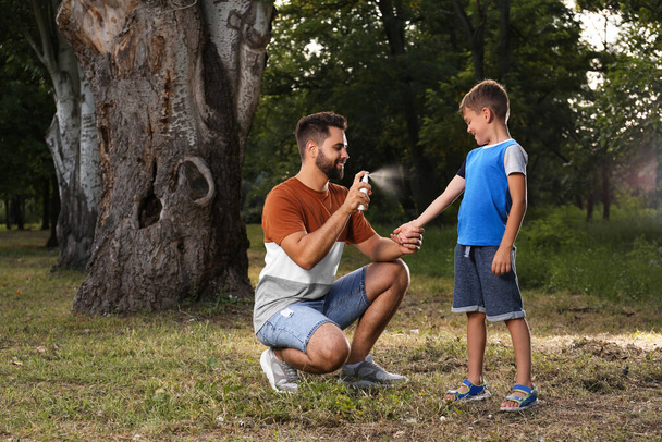 Hombre aplicando repelente de insectos en la pierna de su hijo en el parque. garrapata muerde prevención - Foto, Imagen