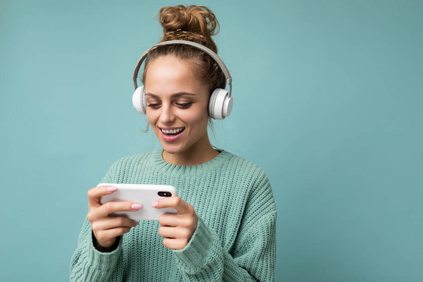 Photo shot of beautiful joyful smiling young female person wearing stylish casual outfit isolated over colorful background wall wearing white bluetooth wireless earphones and listening to music and - Valokuva, kuva