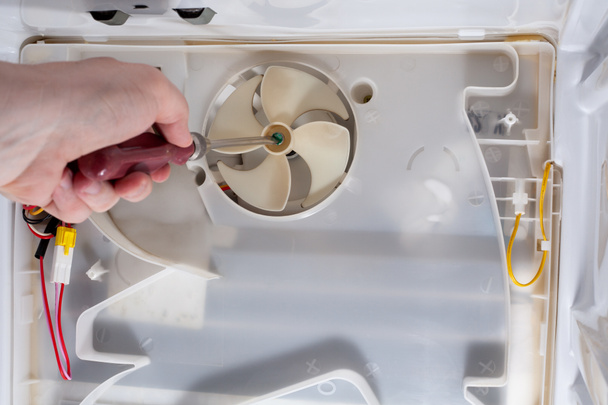 A technician uses a screwdriver in refrigerator fridge. Inside refrigerator repair. Disassembled refrigerator. Removed back cover fridge. fan repair. - Photo, Image