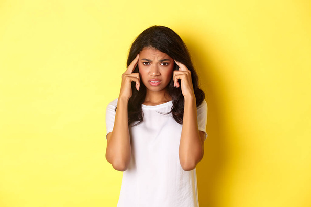 Портрет розчарованої афро-американської дівчини, що кидається і торкається голови, виглядає засмученою на камеру, стоїть над жовтим тлом
 - Фото, зображення