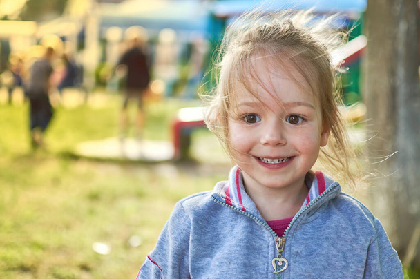Adorabile sorridente bambina nel parco con parco giochi sullo sfondo - Foto, immagini