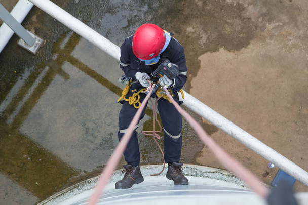 Vista superior inspección de acceso de cuerda de trabajador masculino de la industria de tanques de almacenamiento de espesor por debajo del aceite de tubería - Foto, imagen