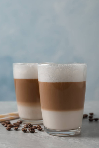 Glasses of delicious layered coffee and beans on grey marble table against light background, space for text - Foto, Imagem
