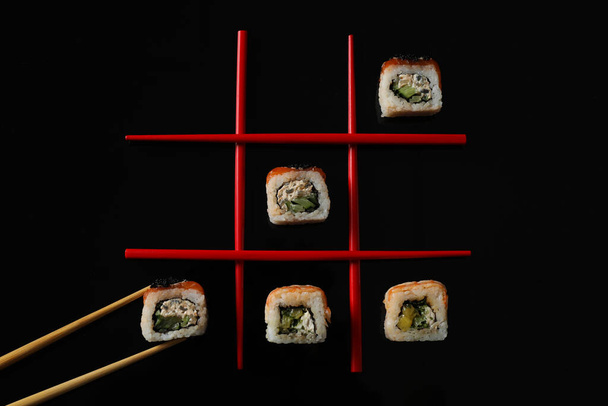 Tic-tac-toe game made with delicious sushi rolls and chopsticks on black background, flat lay - Foto, Imagem