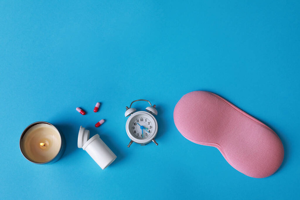 Sleeping mask, pills, candle and alarm clock on light blue background, flat lay. Insomnia treatment - Foto, imagen