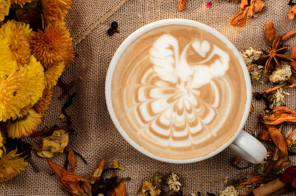 Капучино кава з красивим візерунком на піні в білій чашці на тлі мішковини, прикрашеної спеціями. Вид зверху
 - Фото, зображення