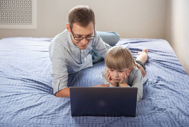 a little boy and his dad watch a movie together online on a laptop screen, lying on the couch - Valokuva, kuva