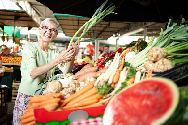 Starší žena vybírá a kupuje zdravou zeleninu na trhu. - Fotografie, Obrázek