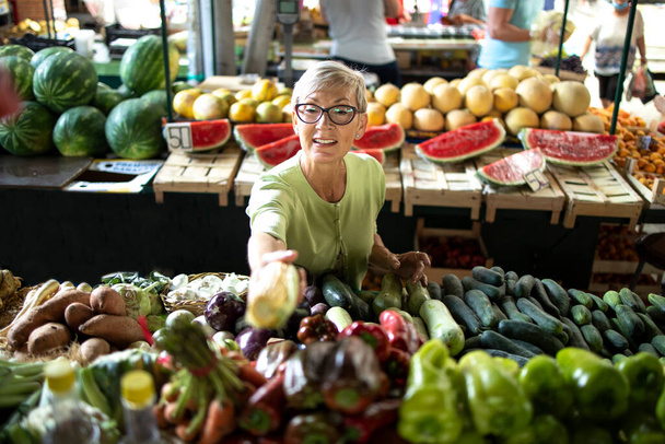 Oudere vrouw koopt verse biologische groenten op de markt voor gezonde voeding. - Foto, afbeelding