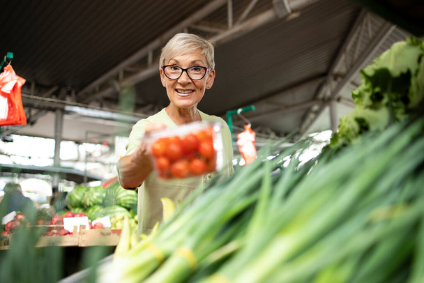 Портрет старшої білої жінки, яка купує свіжі органічні овочі та фрукти на ринку і тримає мішок повний здорової їжі
. - Фото, зображення