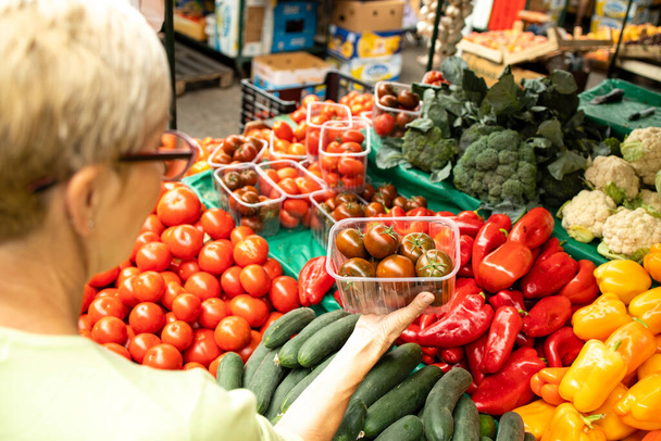 Draufsicht einer älteren kaukasischen Frau, die frisches Bio-Gemüse und -Obst auf dem Marktplatz kauft und eine Tasche voller gesunder Lebensmittel in der Hand hält. - Foto, Bild