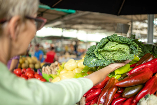 Starší běloška nakupující čerstvou ekologickou zeleninu a ovoce na tržišti a držící tašku plnou zdravých potravin. - Fotografie, Obrázek