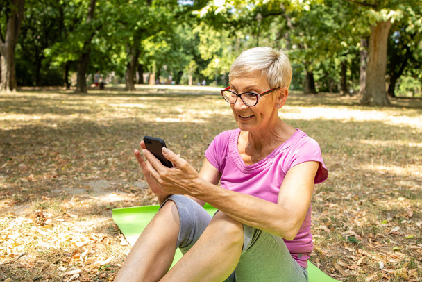 Donna caucasica anziana che utilizza l'applicazione di salute dello smartphone per l'allenamento in natura. - Foto, immagini