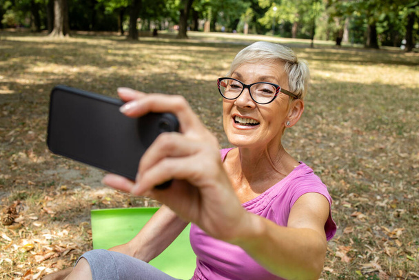 Seniorin benutzt Smartphone und macht Selfie nach dem Training. - Foto, Bild