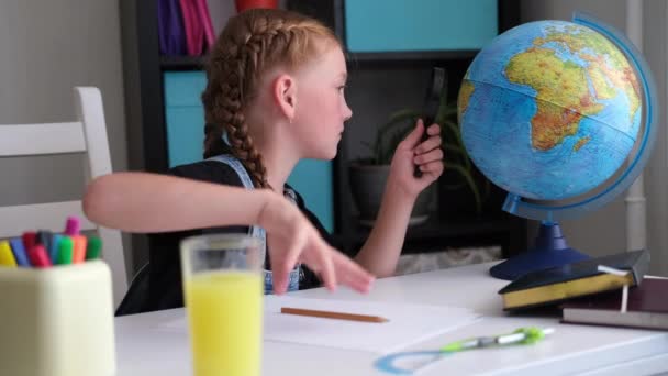 Σοβαρή Καυκάσια κοκκινομάλλα κοπέλα σπουδάζει στο σπίτι, κοιτάζοντας την υδρόγειο - Πλάνα, βίντεο