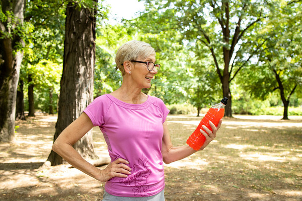 Oudere vrouw klaar voor training met energiedrank in het park. - Foto, afbeelding