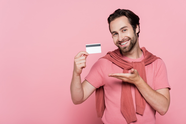 Smiling man pointing at credit card isolated on pink  - Photo, Image