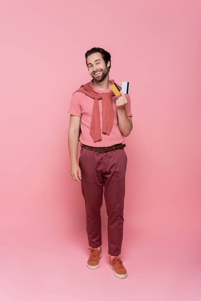 Cheerful man holding credit cards and looking at camera on pink background  - Fotografie, Obrázek