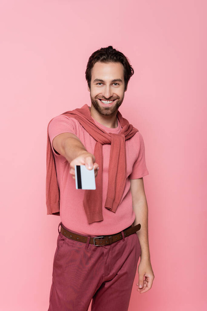 Smiling man holding blurred credit card isolated on pink  - Photo, Image