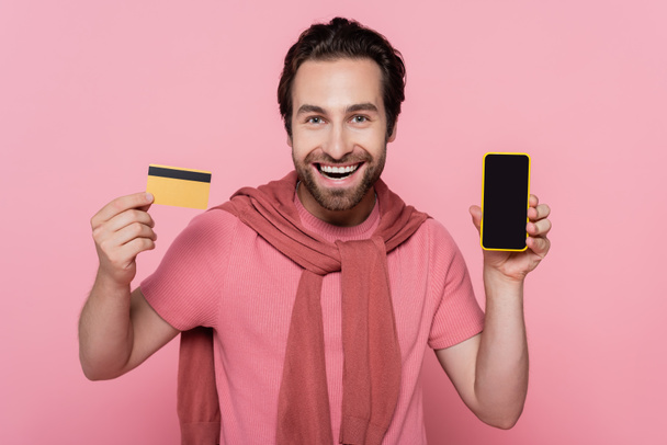 スマートフォンとクレジットカードをピンクに隔離した笑顔の男  - 写真・画像