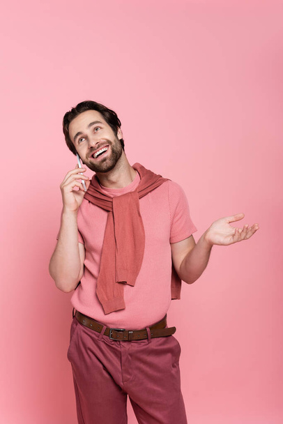 Positive man looking up while talking on smartphone isolated on pink  - Photo, image