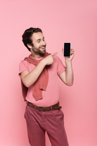 Smiling man pointing at smartphone with blank screen isolated on pink  - Foto, Imagen