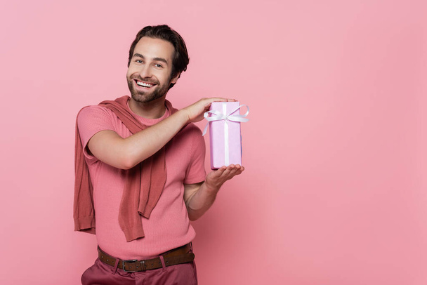 Smiling man holding gift box with ribbon isolated on pink  - Fotografie, Obrázek