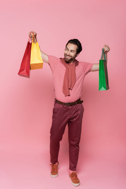Full length of cheerful customer looking at shopping bags on pink background - 写真・画像