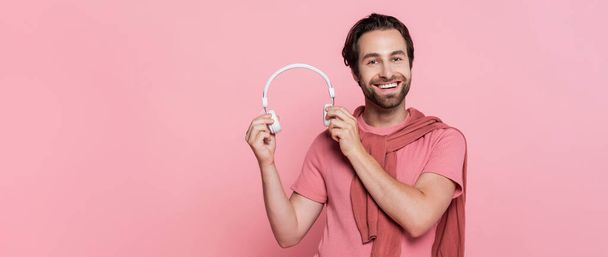 Young man with headphones looking at camera isolated on pink, banner  - Foto, Imagen