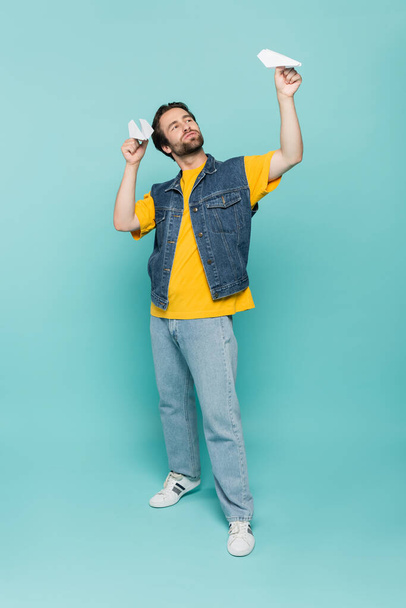 Full length of man playing with paper planes on blue background  - Fotoğraf, Görsel