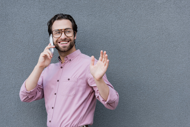 Mosolygó üzletember beszél okostelefonon és integető kéz  - Fotó, kép