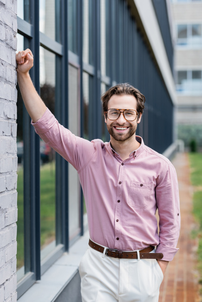 Hombre de negocios sonriente con anteojos y camisa de pie cerca del edificio  - Foto, Imagen
