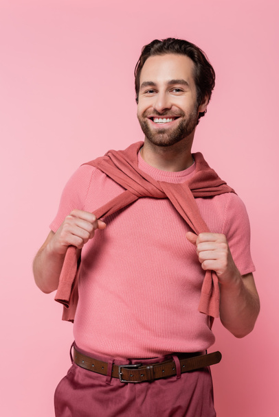 Cheerful man holding jumper on shoulders isolated on pink - Φωτογραφία, εικόνα