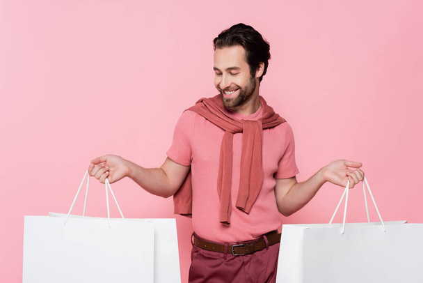 Young man smiling while looking at shopping bag isolated on pink - Fotoğraf, Görsel