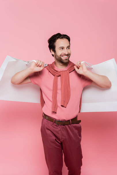 Smiling shopaholic holding shopping bags isolated on pink - Фото, изображение