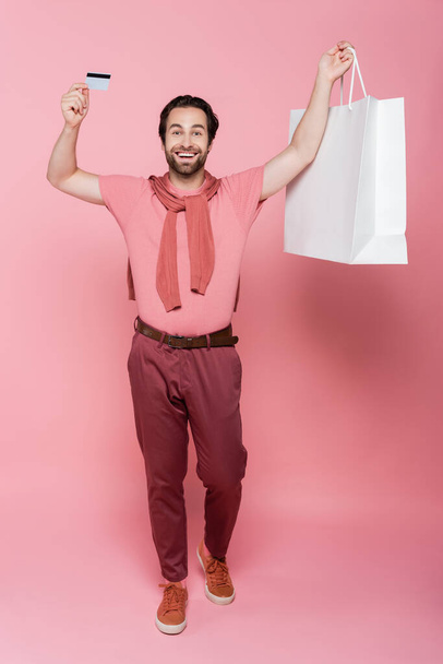 Podekscytowany człowiek z kartą kredytową i torbą na zakupy na różowym tle - Zdjęcie, obraz