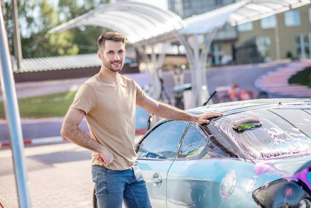 Smiling man standing near automobile at car wash - Fotoğraf, Görsel
