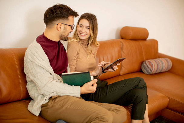 Jóképű fiatal pár, akik digitális táblagépet használnak, miközben otthon ülnek a kanapén - Fotó, kép