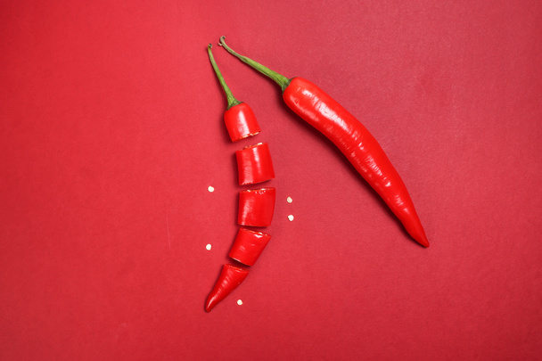 hele rode chili peper op rood papier achtergrond gesneden stukken zaden - Foto, afbeelding