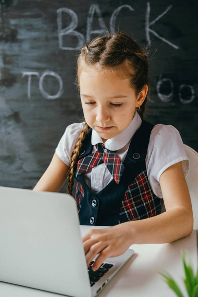 Cute little school girl sitting at the desk and using computer. Back to school and online lessons concept. - Φωτογραφία, εικόνα